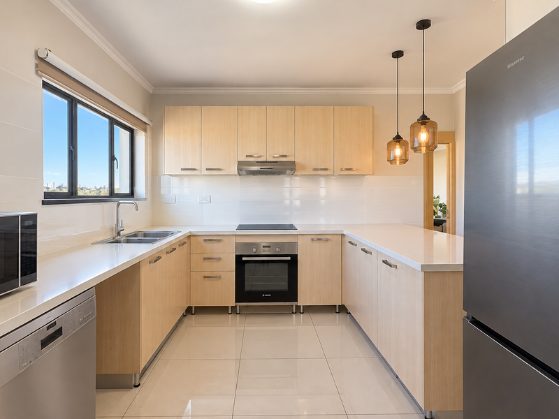 Modern kitchen featuring light-wood cabinetry, stone countertops, integrated appliances, and sleek tiled flooring with ample natural light.