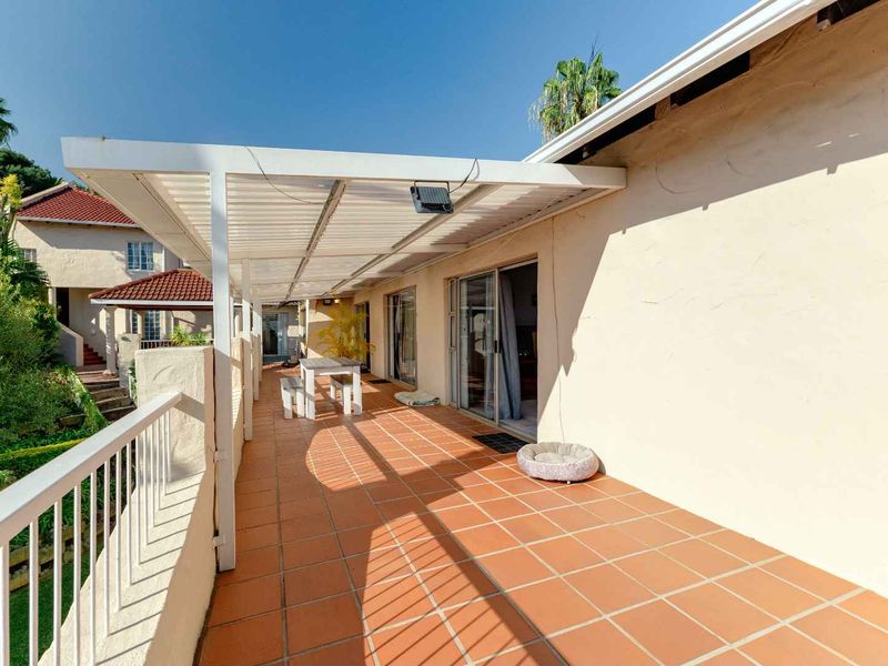 A spacious covered patio featuring terracotta tiling, a white metal pergola, and direct access to the interior through sliding glass doors.