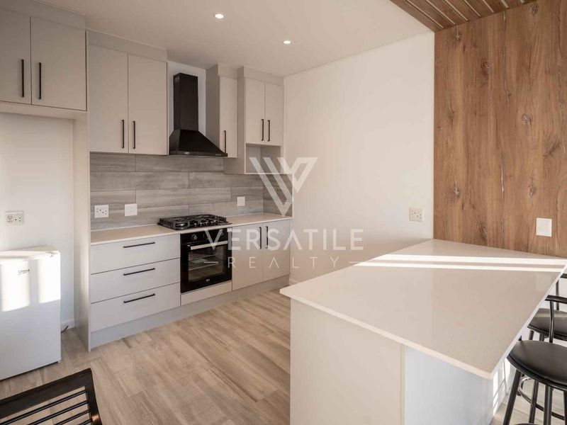 Modern kitchen featuring sleek cabinetry, stone countertops, a gas hob with extractor, and a functional breakfast island with integrated lighting.