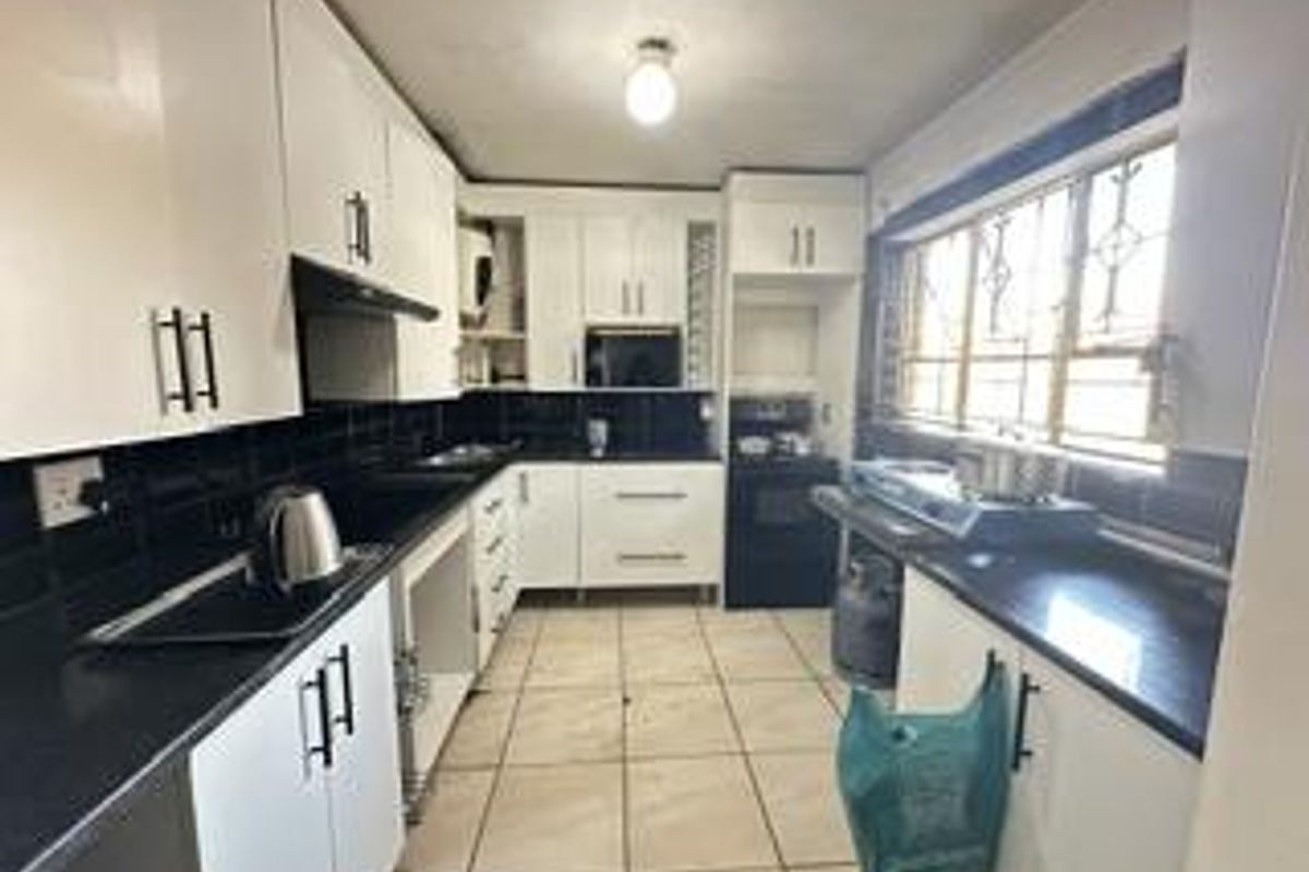 A functional kitchen featuring white cabinetry, black countertops, tiled splashbacks, and a window with security bars.