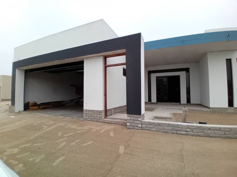 Front elevation of a modern house under construction, featuring a garage, covered entrance, and unfinished landscaping.