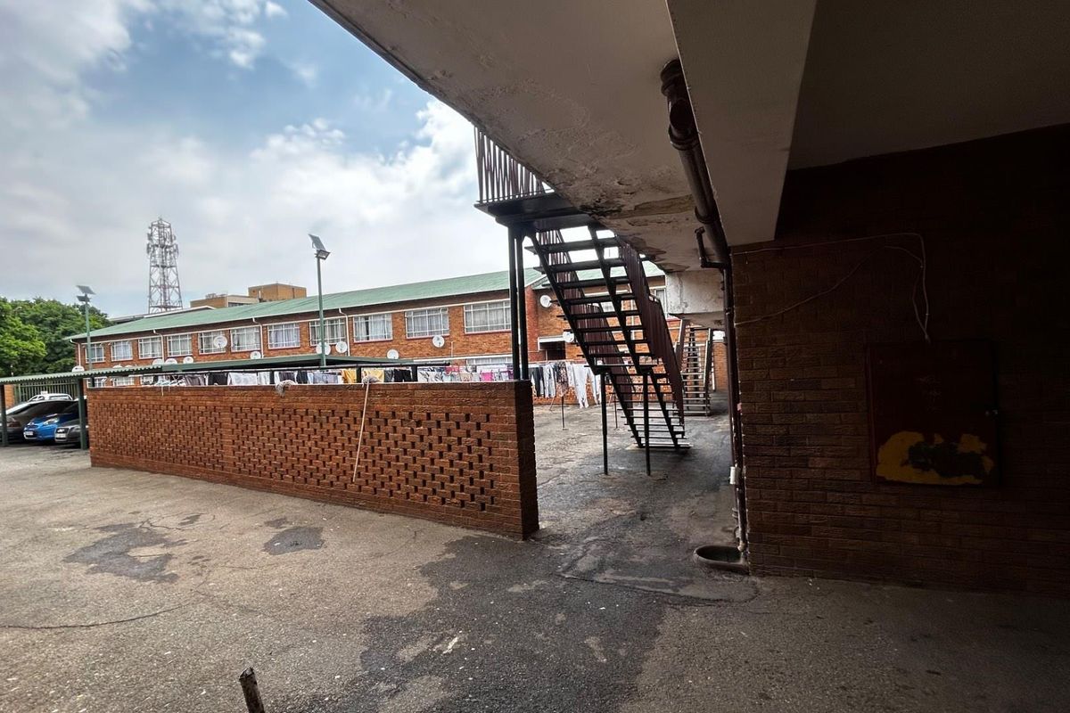 Exterior view of an apartment complex courtyard featuring a brick boundary wall, metal staircase, and paved communal area.