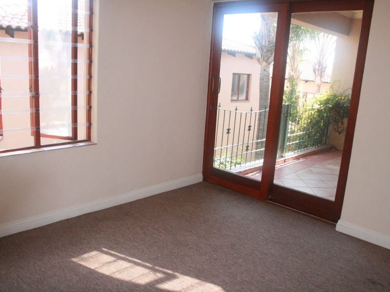 An empty bedroom featuring carpeted flooring, a louvered window, and a sliding glass door providing access to an outdoor balcony area.