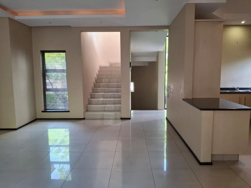Spacious open-plan living area featuring polished tile flooring, a modern staircase, and a kitchen breakfast bar with granite countertops.