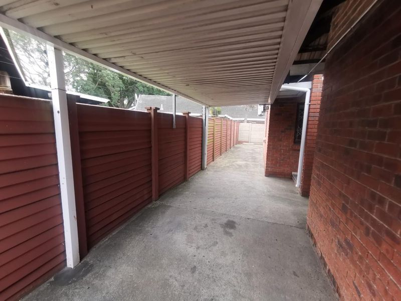 A covered carport area featuring concrete flooring and brick wall boundaries, providing secure outdoor parking space.