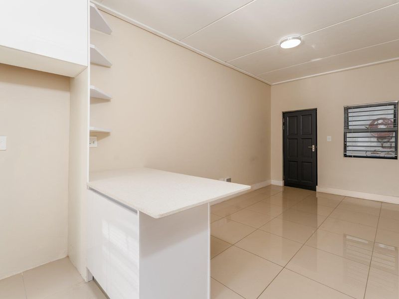 A clean, empty kitchen area featuring tiled flooring, built-in cabinetry with a stone countertop, and neutral wall finishes.