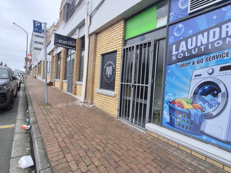 Street-level view of a commercial storefront featuring brick exterior, security gates, and large display windows along a paved sidewalk.