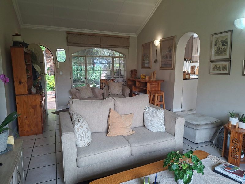 A cozy living room featuring tiled floors, a vaulted ceiling, and an arched doorway leading to the kitchen area, with natural light from a large window.