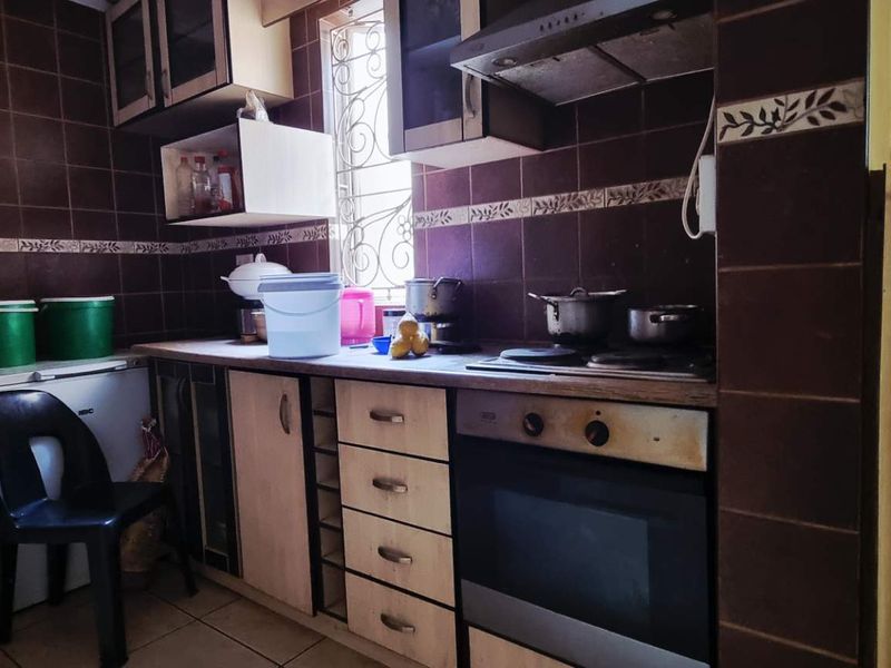 A functional kitchen featuring built-in cabinetry, an integrated oven and hob, and dark tiled splashbacks, offering potential for a modern cosmetic update.