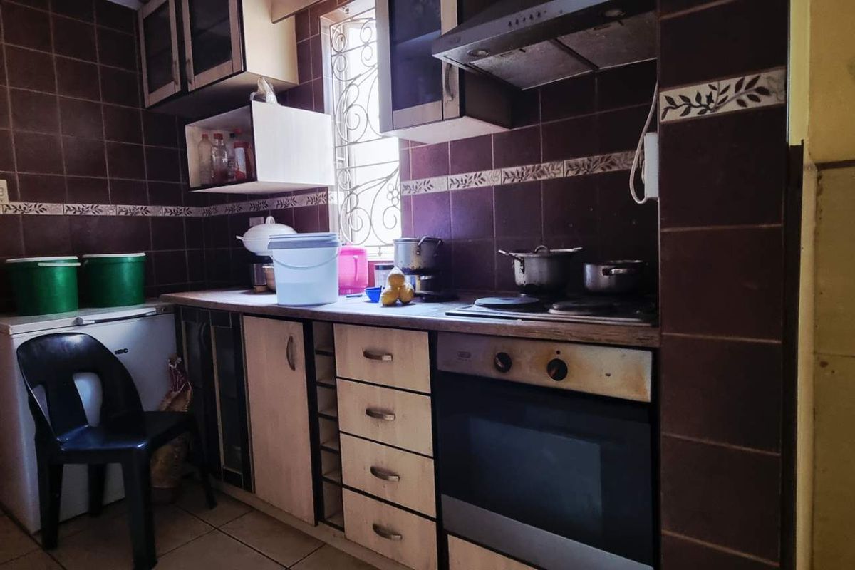 A functional kitchen featuring built-in cabinetry, an integrated oven and hob, and dark tiled splashbacks, offering potential for a modern cosmetic update.