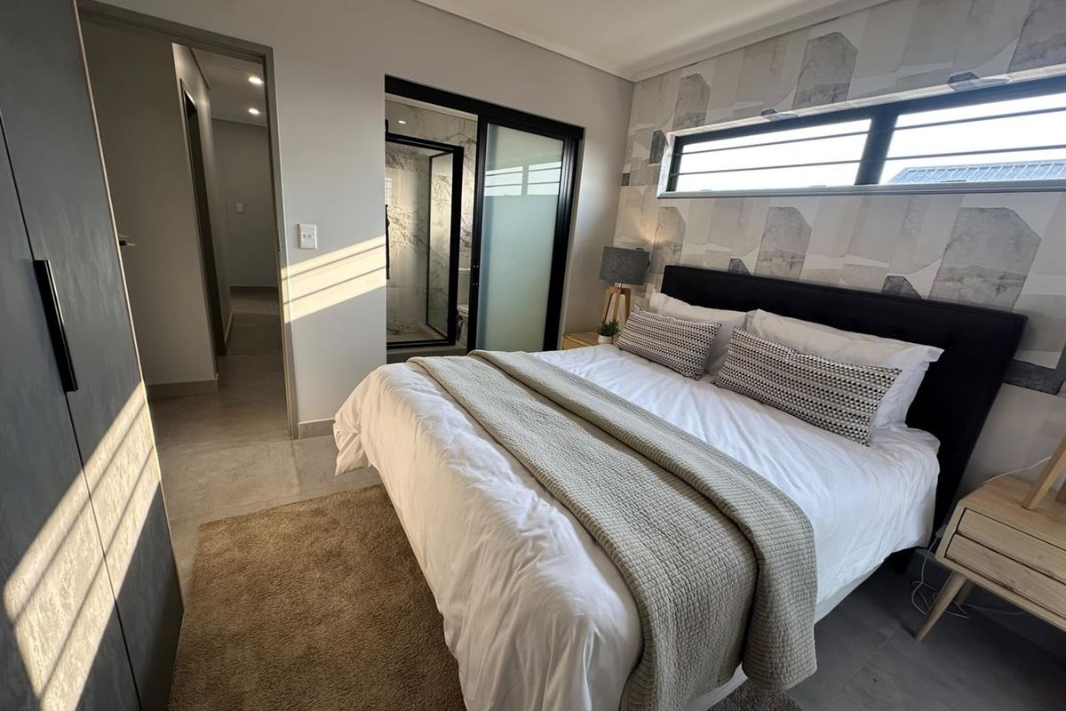 Modern bedroom featuring tiled flooring, built-in cupboards, and an en-suite bathroom with a sliding door entrance.