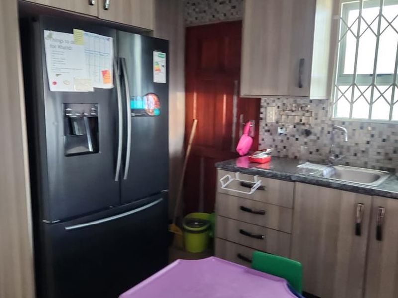 A functional kitchen featuring light wood-tone cabinetry, granite-look laminate countertops, a tiled backsplash, and a window with security bars.