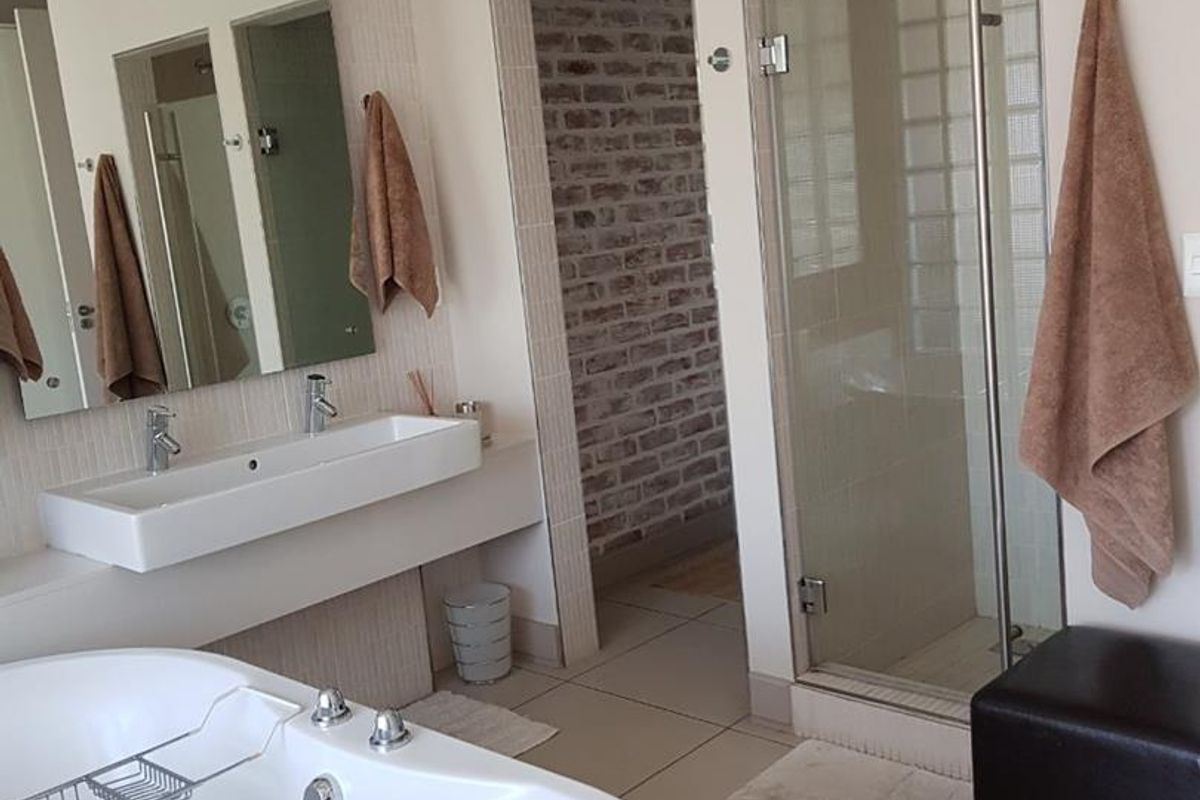 Modern bathroom featuring a freestanding bathtub, wall-mounted vanity with dual basins, and a separate glass-enclosed shower with exposed brick feature wall in the background.
