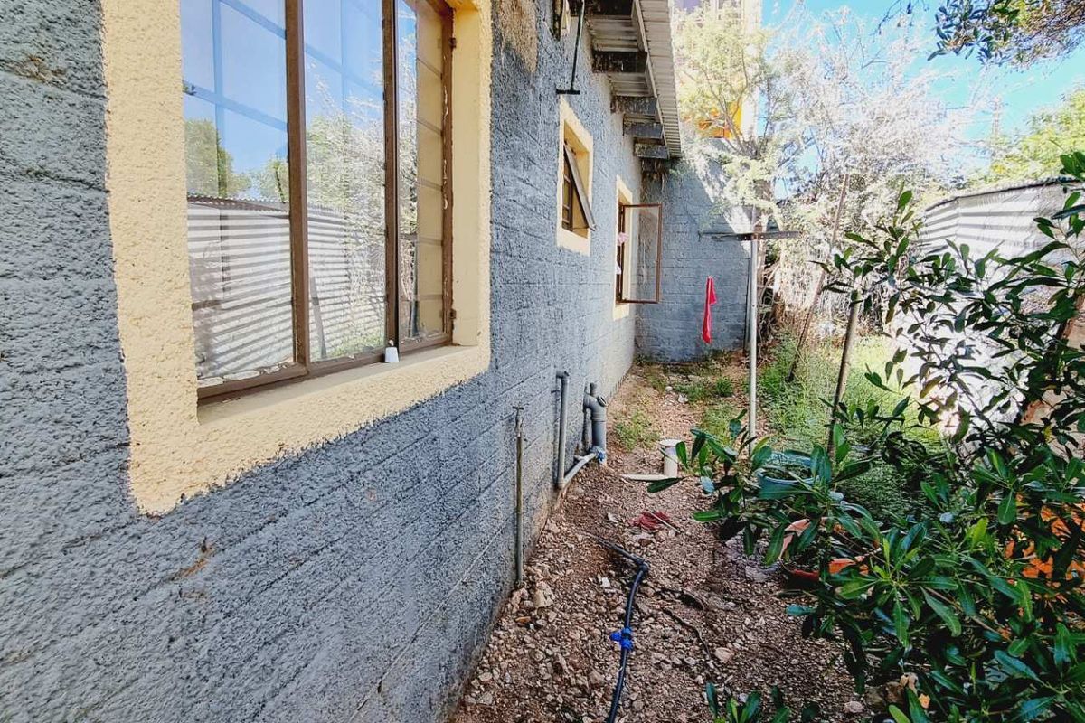 A view of the rear exterior of the house showing textured masonry walls, metal window frames, and an unlandscaped side yard area.