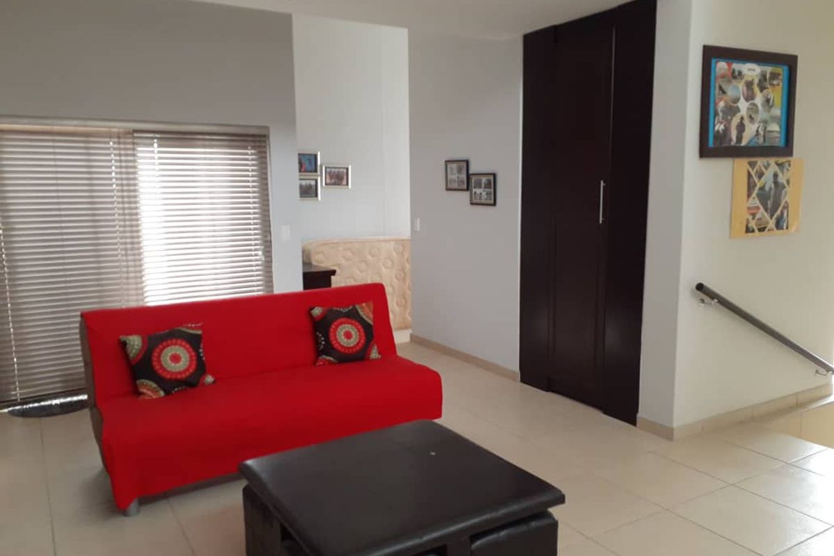A living area featuring tiled flooring, a built-in dark wood storage cupboard, and a staircase with a metal handrail.