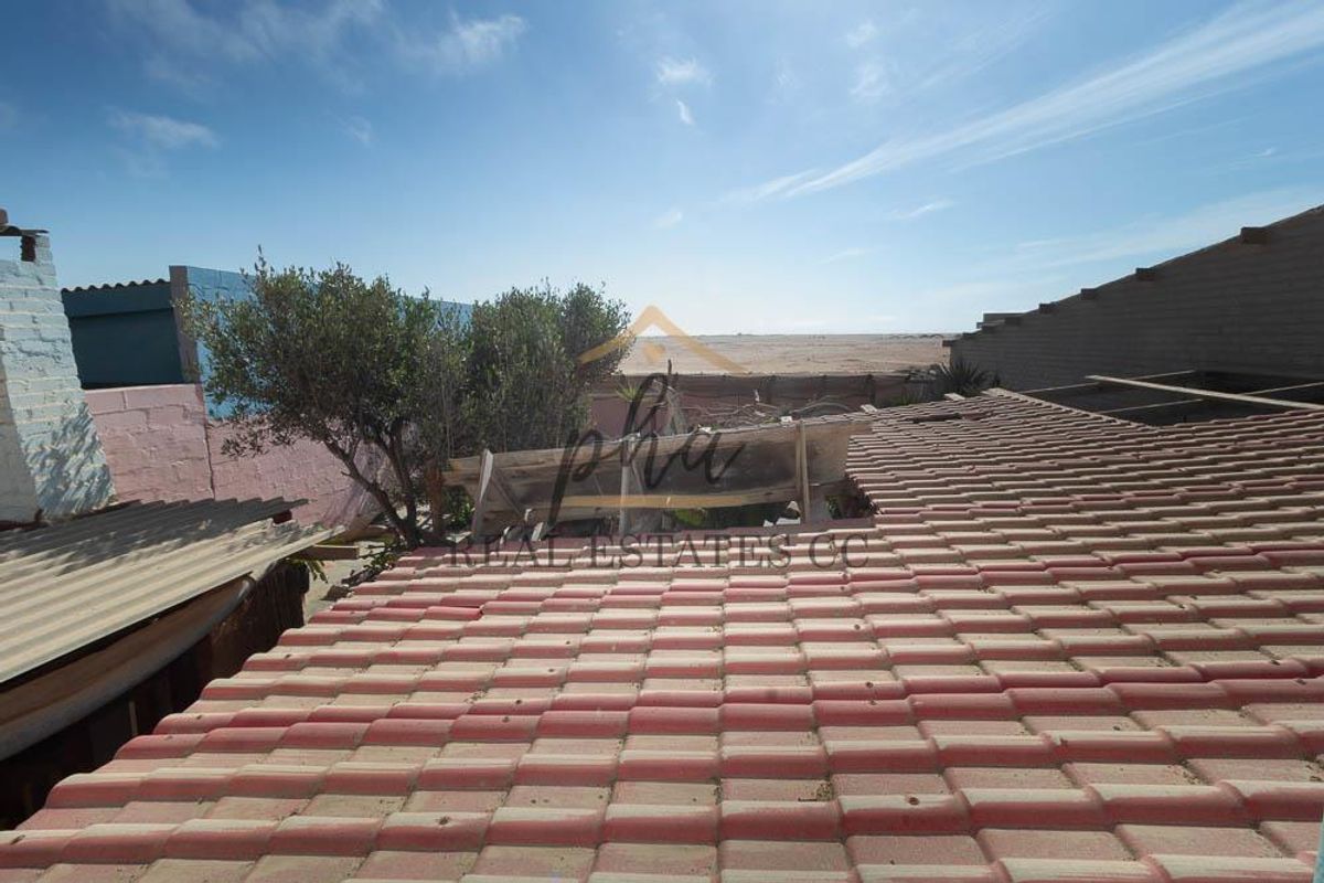An elevated view of a rear exterior area featuring a tiled roof structure in need of maintenance and a view towards the horizon.