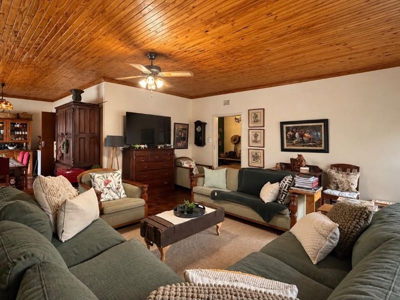 Spacious living room featuring a warm timber tongue and groove ceiling, ceiling fan, and classic parquet flooring, creating a cozy and traditional atmosphere.