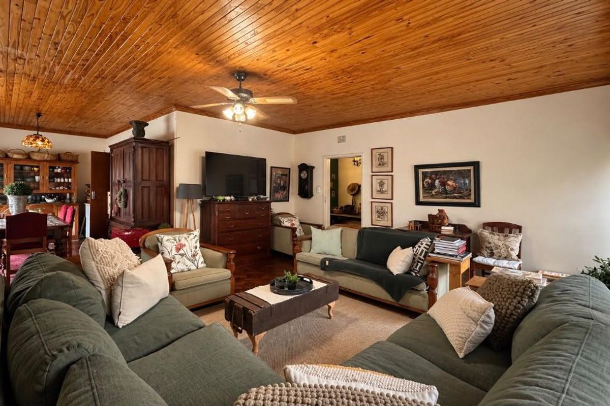 Spacious living room featuring a warm timber tongue and groove ceiling, ceiling fan, and classic parquet flooring, creating a cozy and traditional atmosphere.