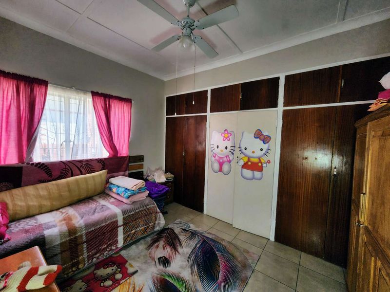 A bedroom featuring tiled flooring, a ceiling fan, and extensive built-in wooden cupboards providing ample storage space.