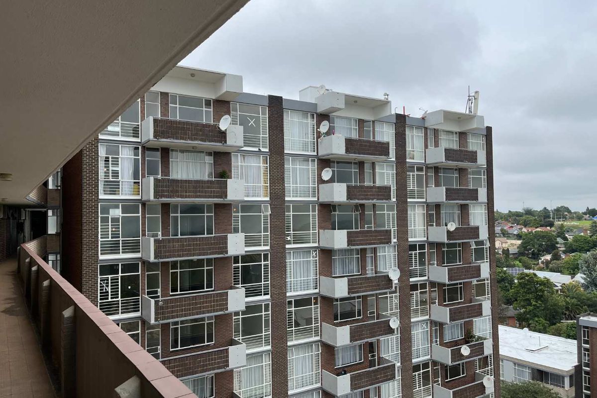 View of a multi-story apartment building facade featuring brick exterior, private balconies, and large windows from an adjacent balcony.