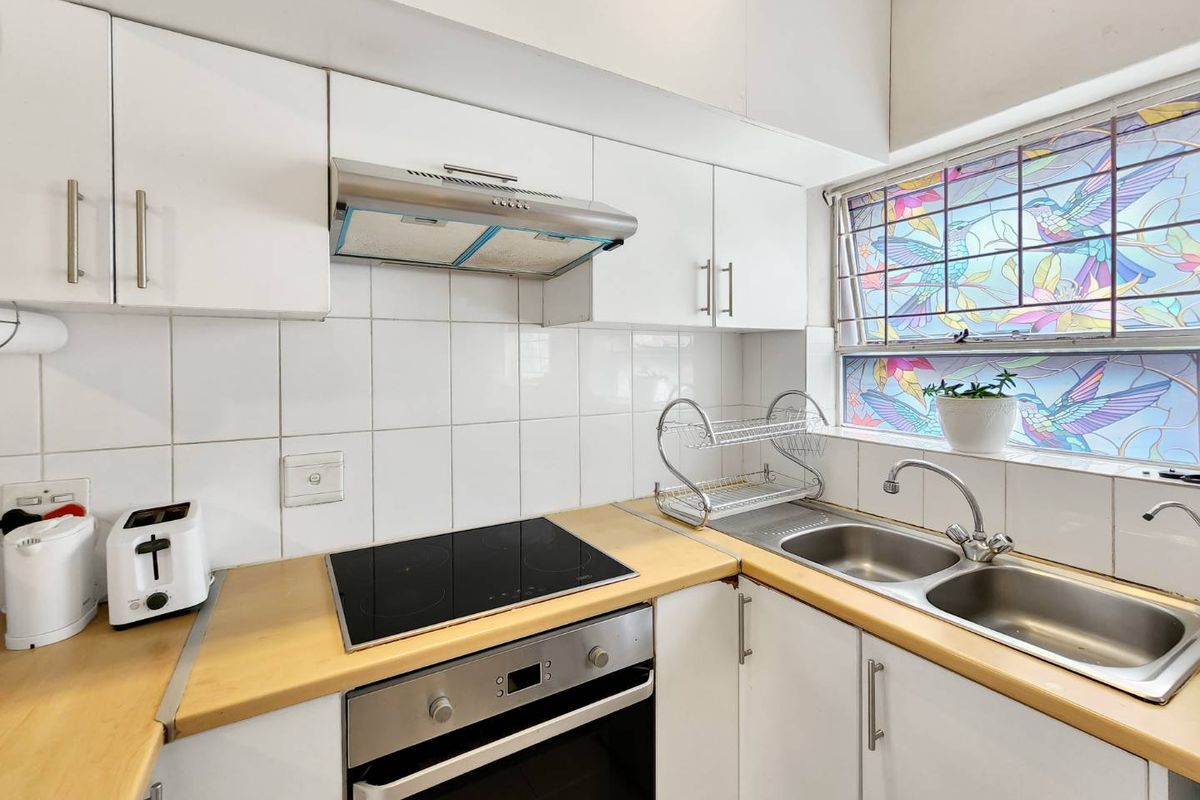 Compact kitchen featuring white cabinetry, a built-in oven, electric hob, stainless steel extractor fan, and a double basin sink with decorative window film.
