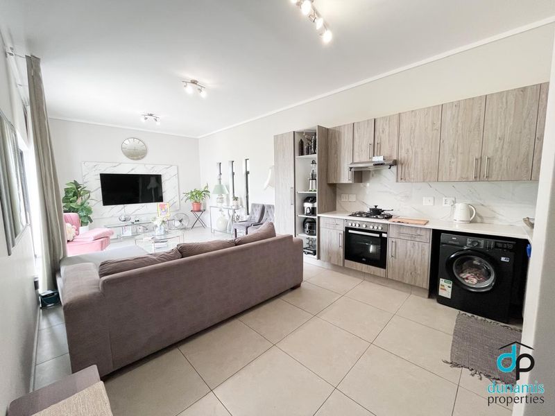 Modern open-plan living area featuring a contemporary kitchen with built-in cabinetry, integrated appliances, and sleek tiled flooring throughout.