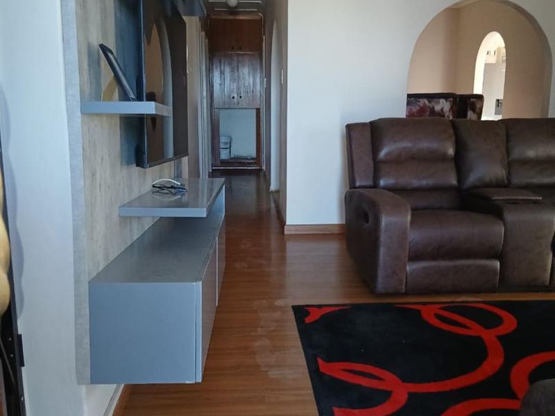 Living room featuring laminate flooring, a built-in media console, and an arched entryway leading to a hallway with built-in storage.