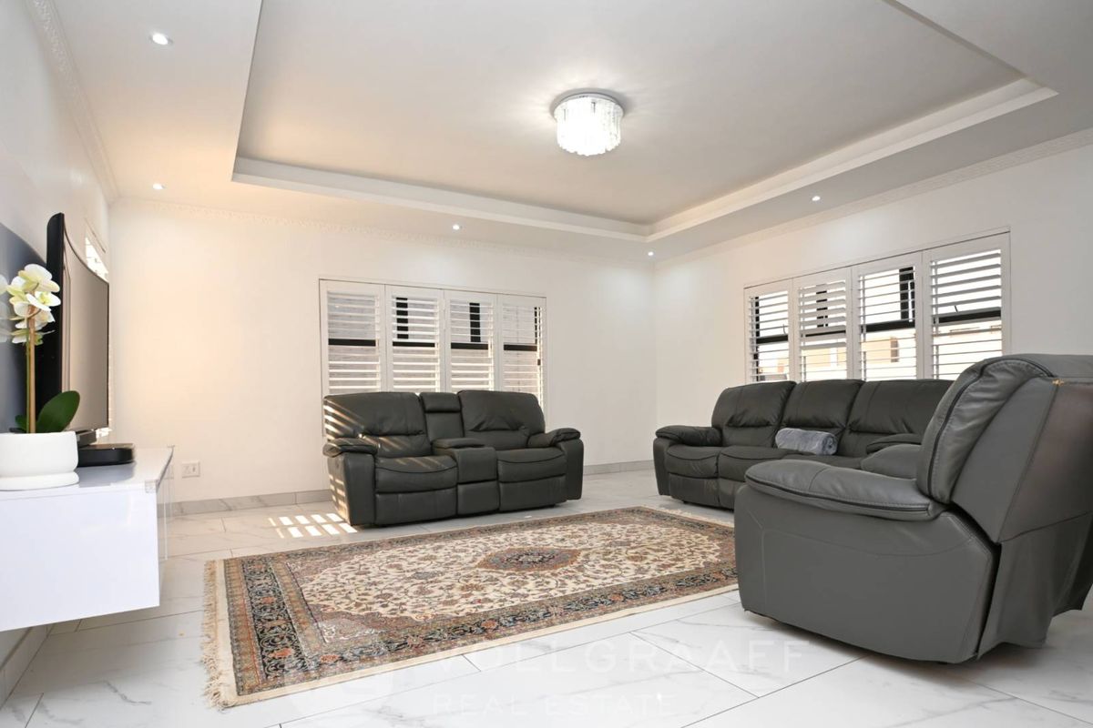 A bright and modern living room featuring tiled floors, a recessed ceiling with downlights, and white plantation shutters.
