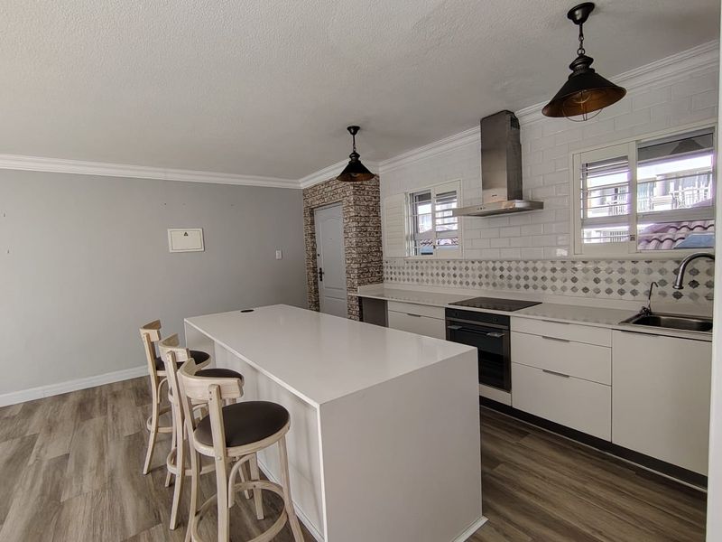 Modern open-plan kitchen featuring a central island, sleek white cabinetry, subway tile backsplash, and integrated appliances, complemented by stylish pendant lighting.