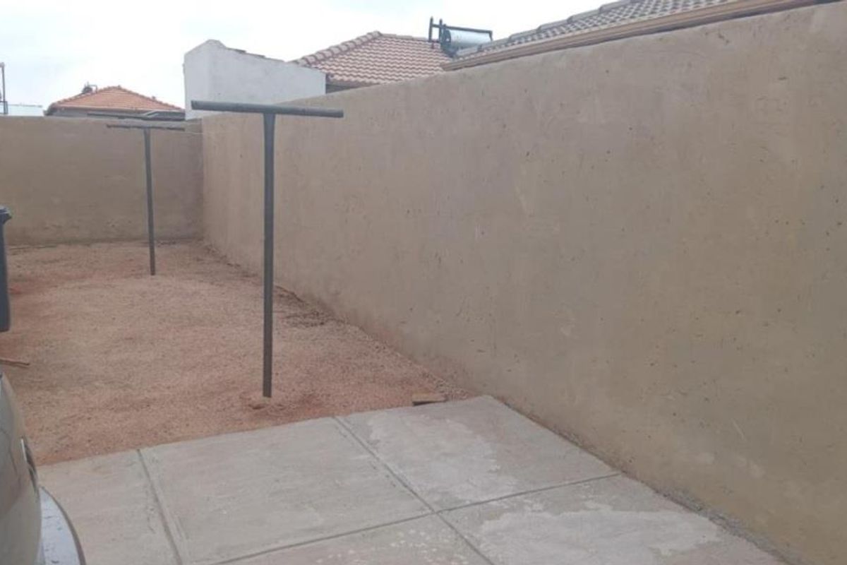 A rear exterior area featuring a concrete paved section, a large perimeter boundary wall, and metal washing line poles.