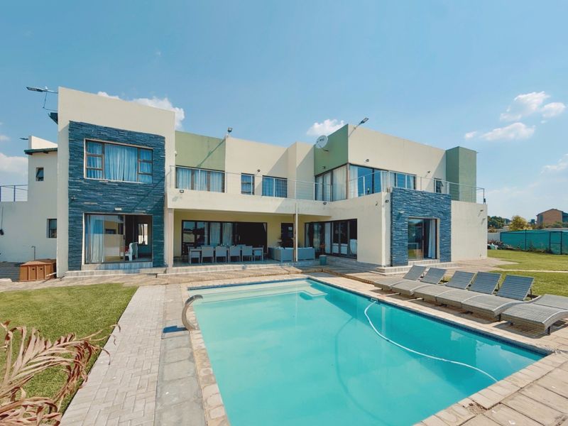 Rear view of a modern double-story home featuring a swimming pool, paved patio area, and stone-clad architectural accents.