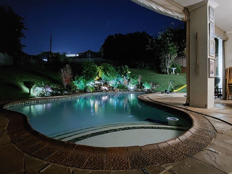 Night view of a swimming pool with integrated lighting, set against a landscaped garden and a covered stone-paved patio area.