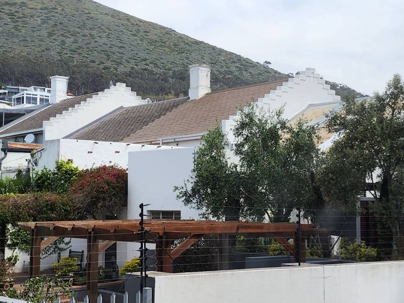Rear view of the property featuring traditional stepped gables, tiled roofing, and a timber pergola set against a mountain backdrop.