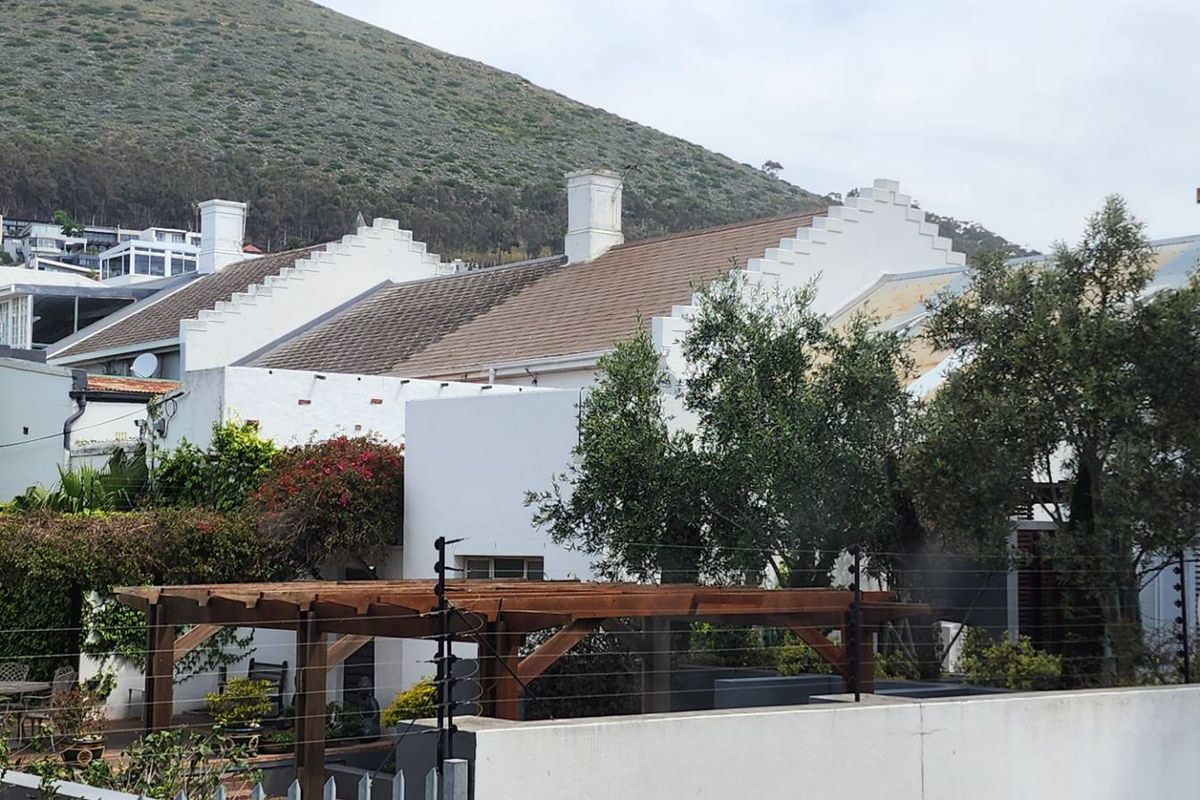 Rear view of the property featuring traditional stepped gables, tiled roofing, and a timber pergola set against a mountain backdrop.