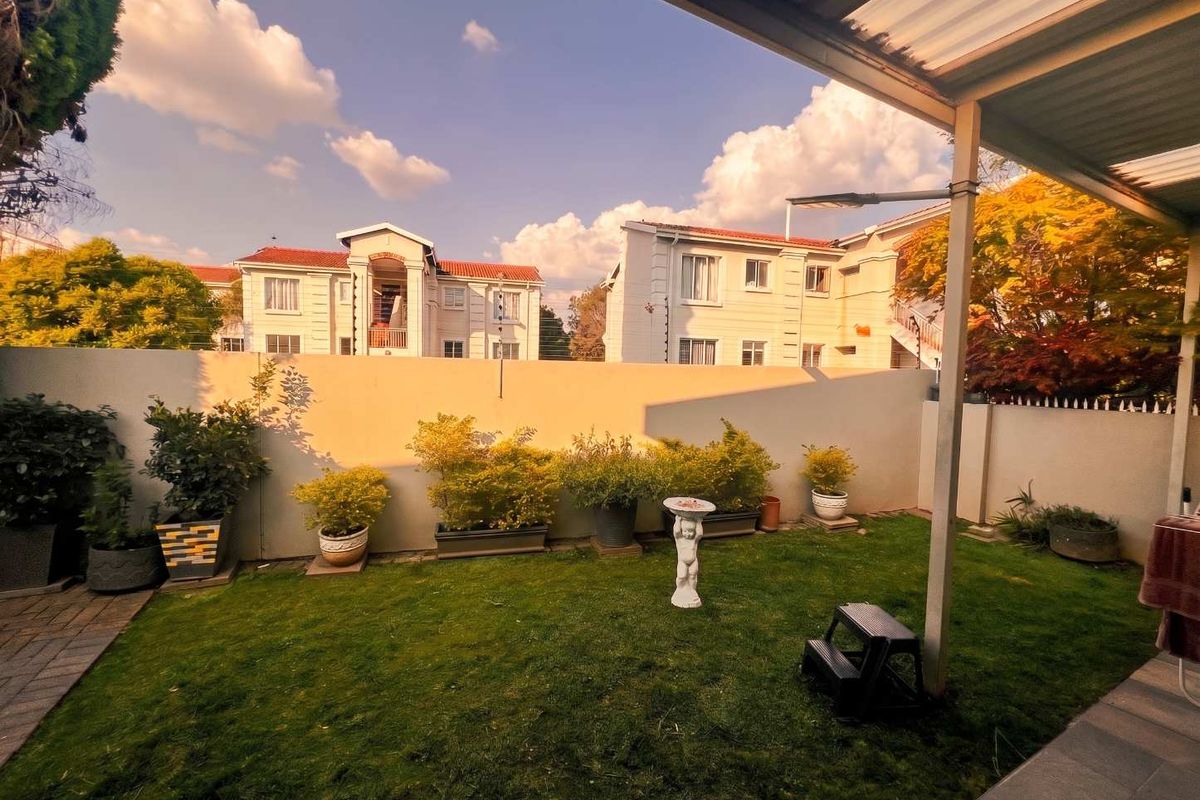 A private rear garden featuring a well-maintained lawn, perimeter wall with electric fencing, and a covered patio area.