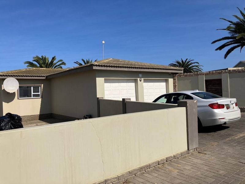 Front exterior view of the property featuring a double garage, paved driveway, and a boundary wall.