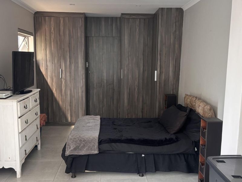 A well-maintained bedroom featuring dark wood-grain built-in cupboards and neutral tiled flooring, providing ample storage and a clean, modern aesthetic.
