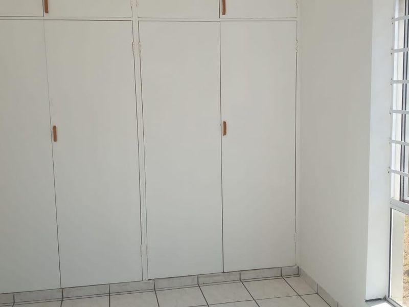 A bright, empty bedroom featuring built-in cupboards, tiled flooring, and a sliding door providing access to the exterior.