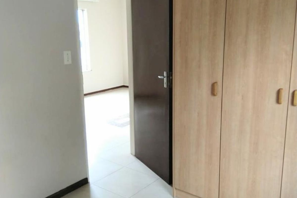 A bedroom featuring light-toned built-in cupboards, tiled flooring, and a doorway leading to an adjacent room.