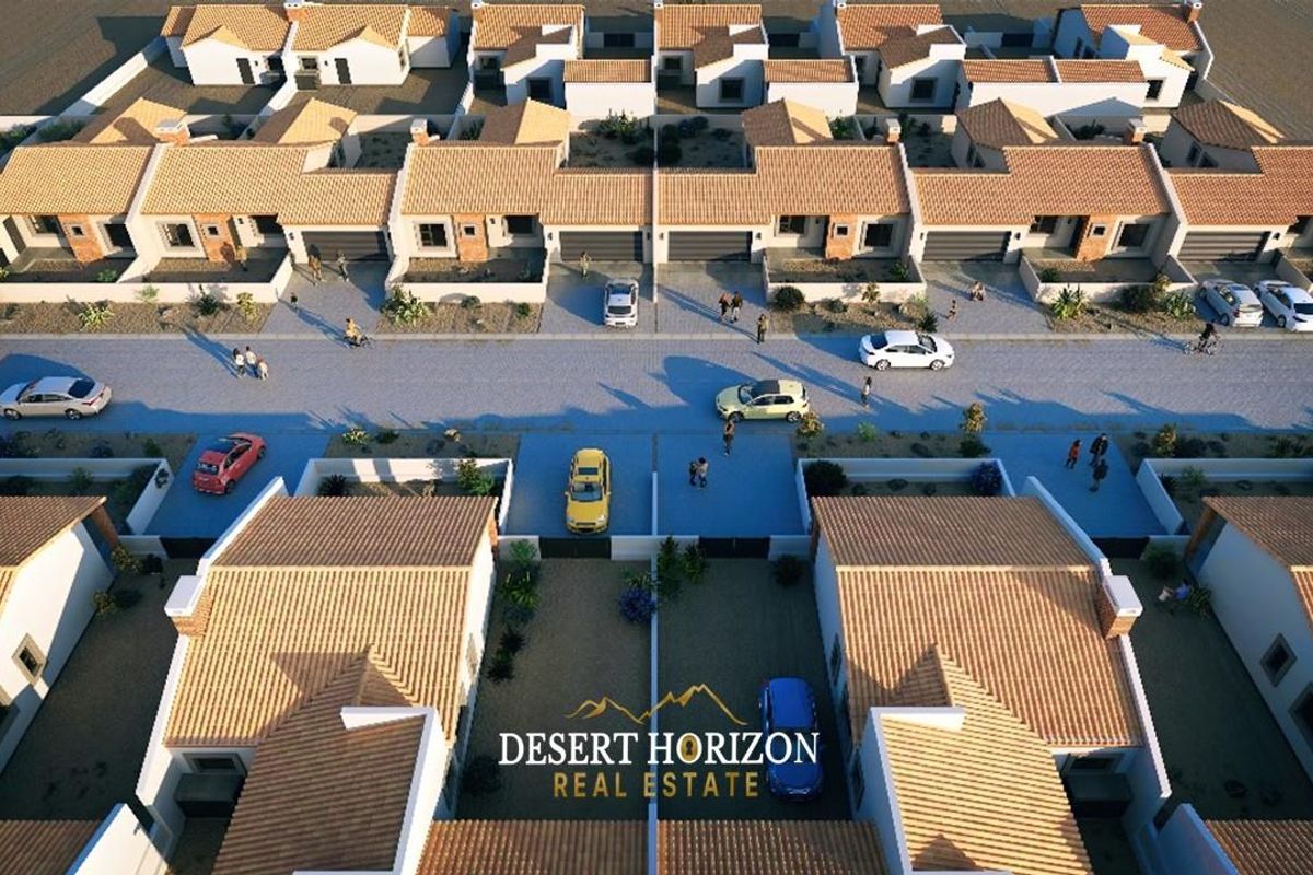 An aerial view of a residential townhouse development featuring uniform architecture, tiled roofs, and paved street access.