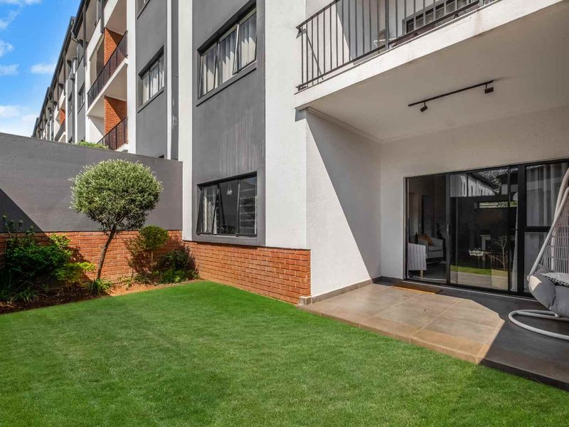 A private ground-floor apartment garden featuring a tiled patio area, sliding door access, and a well-maintained lawn with brick boundary walling.
