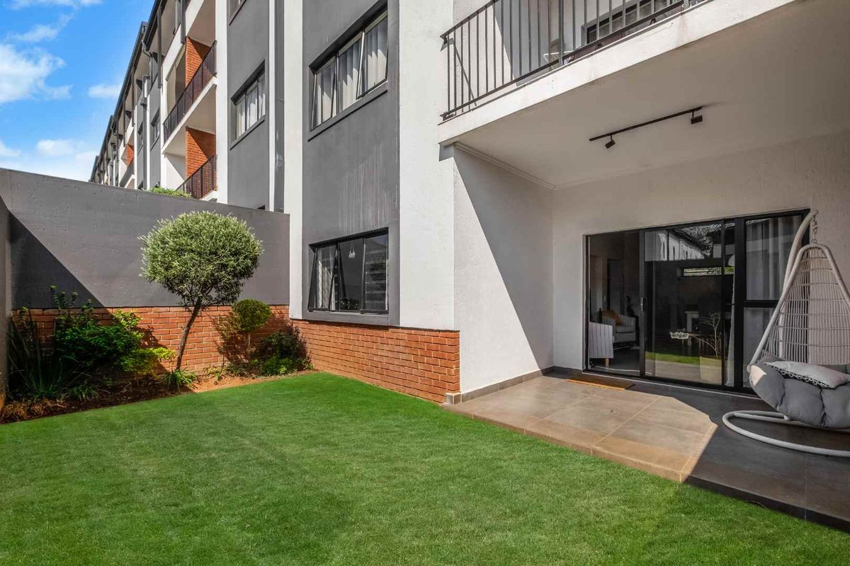 A private ground-floor apartment garden featuring a tiled patio area, sliding door access, and a well-maintained lawn with brick boundary walling.