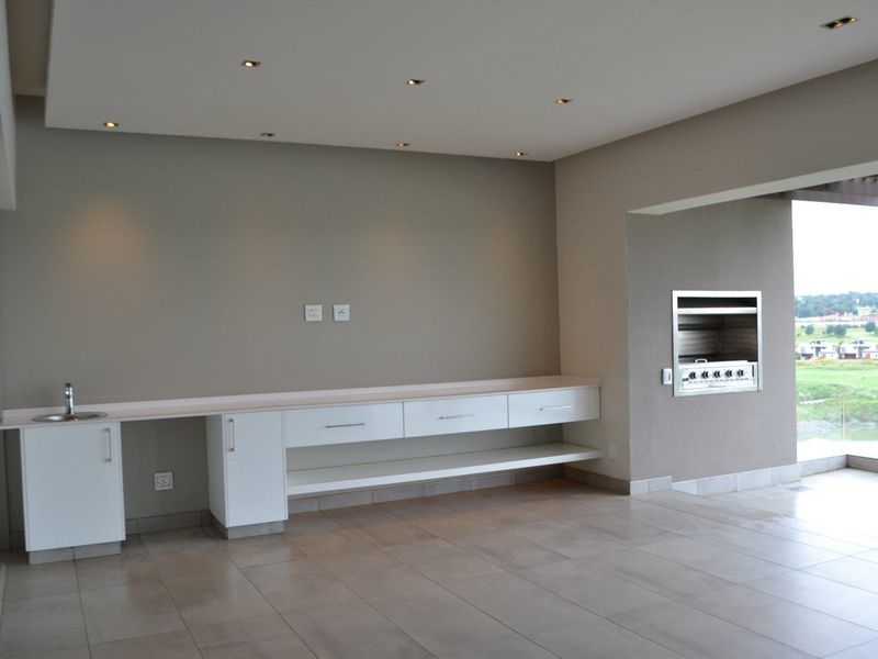 Open plan living area featuring built-in cabinetry with sink and a built-in braai, finished with neutral tiling and recessed lighting.