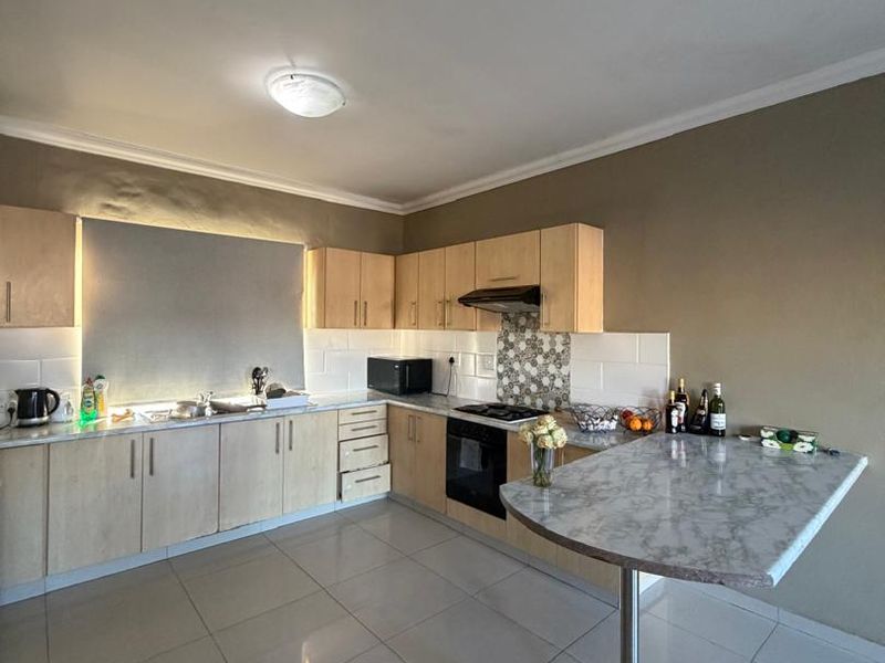 A functional kitchen featuring light wood cabinetry, a breakfast bar, built-in oven with hob, and tiled flooring.