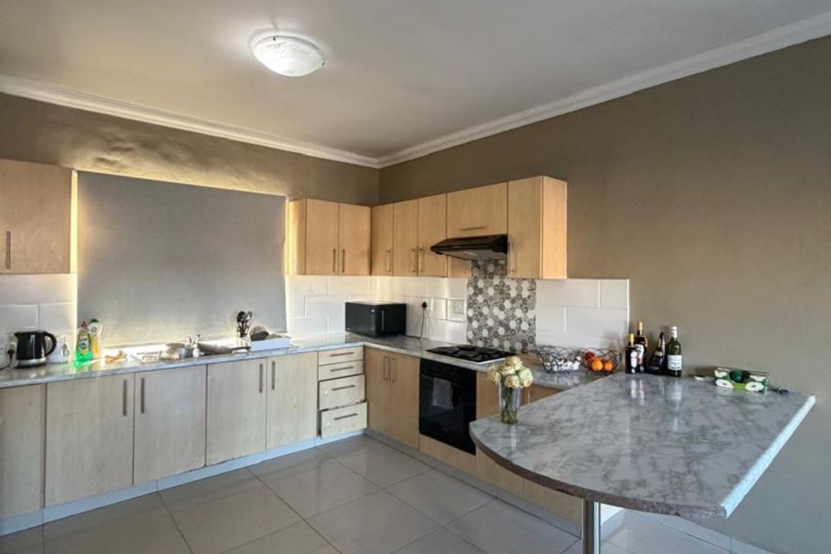 A functional kitchen featuring light wood cabinetry, a breakfast bar, built-in oven with hob, and tiled flooring.