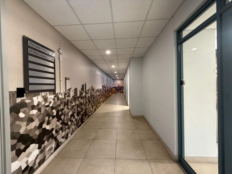 A clean, well-lit commercial hallway featuring tiled flooring, a suspended ceiling, and a decorative wall mural with directional signage.