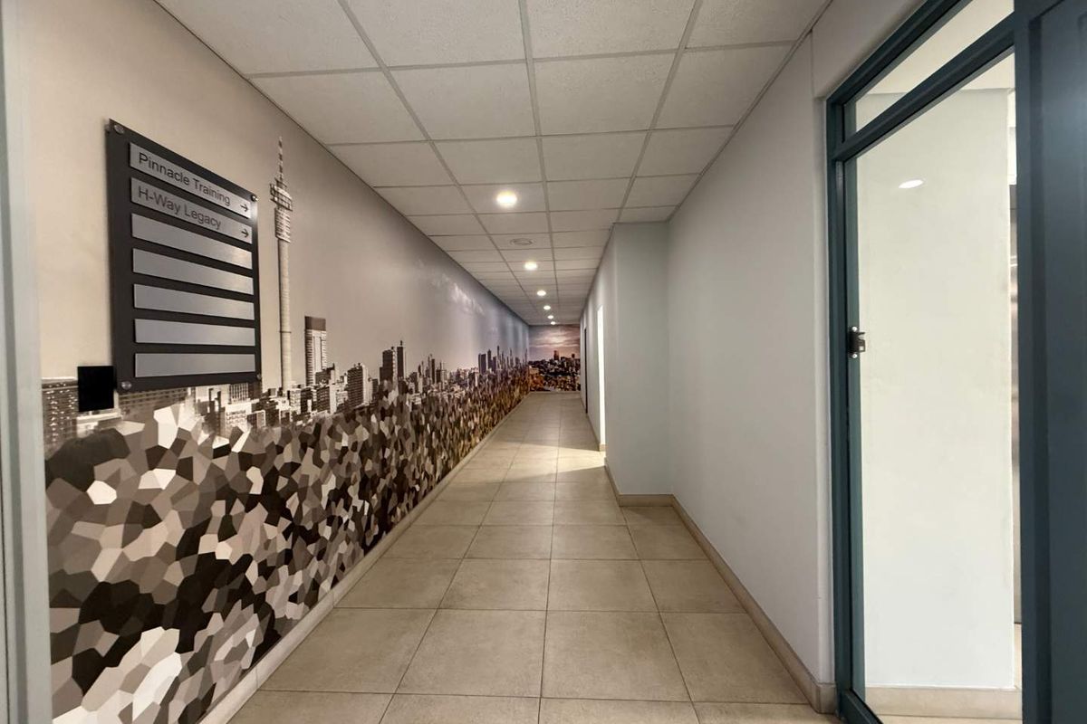 A clean, well-lit commercial hallway featuring tiled flooring, a suspended ceiling, and a decorative wall mural with directional signage.