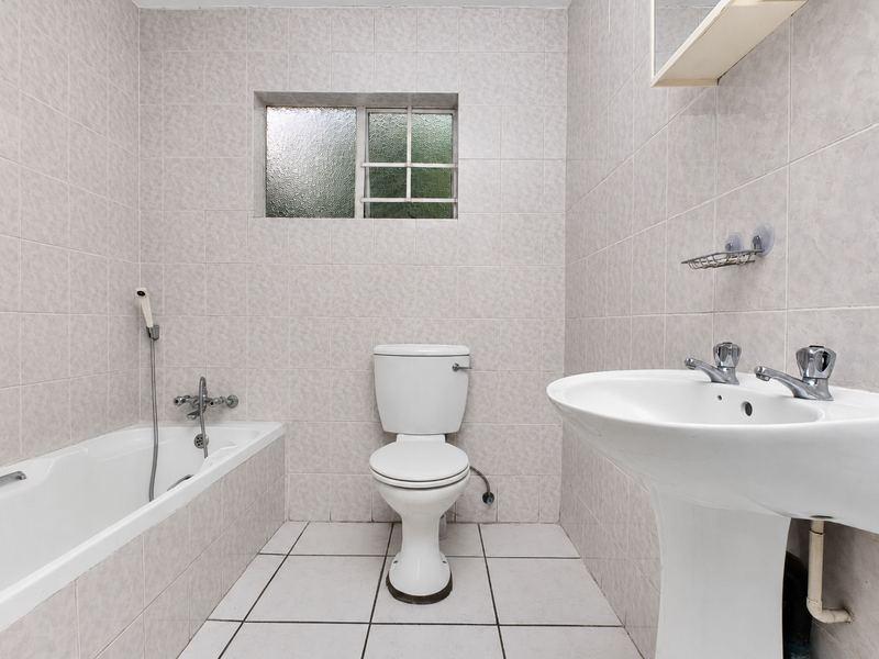 A functional bathroom featuring a pedestal basin, bathtub, and toilet with neutral wall and floor tiling throughout.