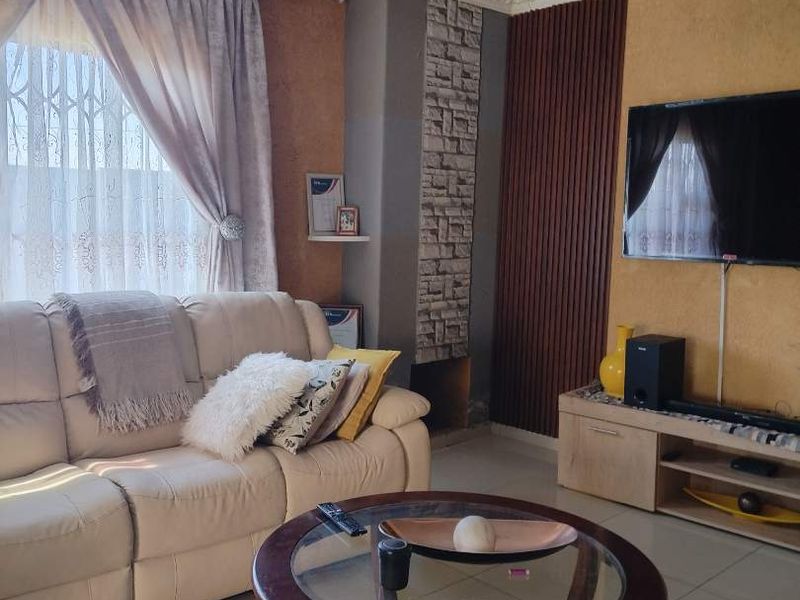 A well-maintained living room featuring tiled floors, decorative stone and timber wall accents, recessed lighting, and a central crystal chandelier.