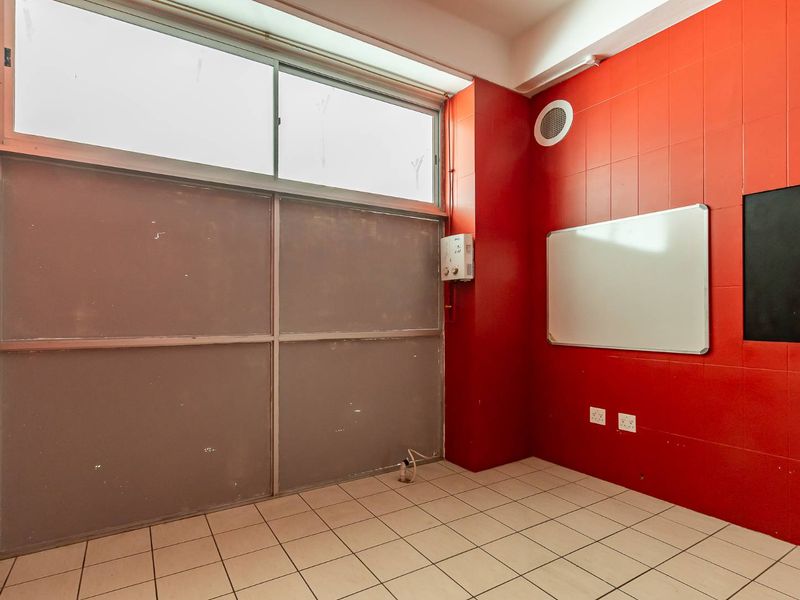 An empty office space featuring bright red tiled walls, light-colored floor tiles, a large sliding window, and wall-mounted electrical and heating fixtures.